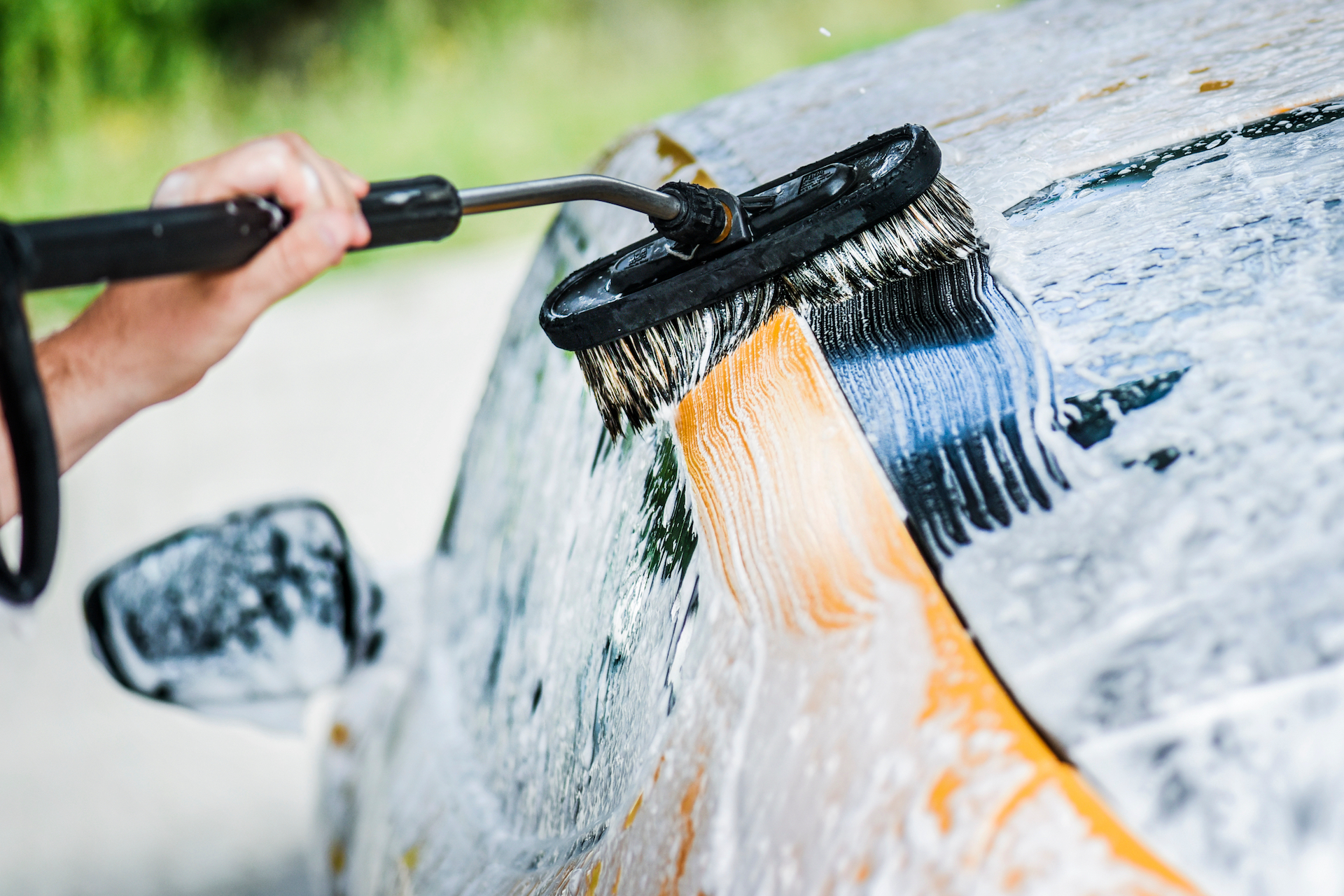 Car washing close up. Cleaning a car with foam brush and high pressure water.
